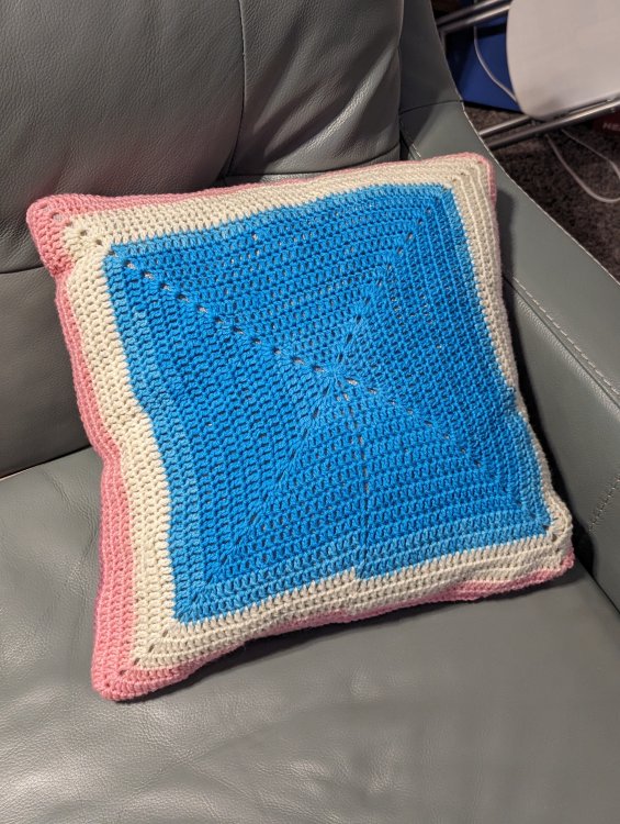 The front part of a crochet pillow cover with blue in the center, then white, then finally pink on the edges