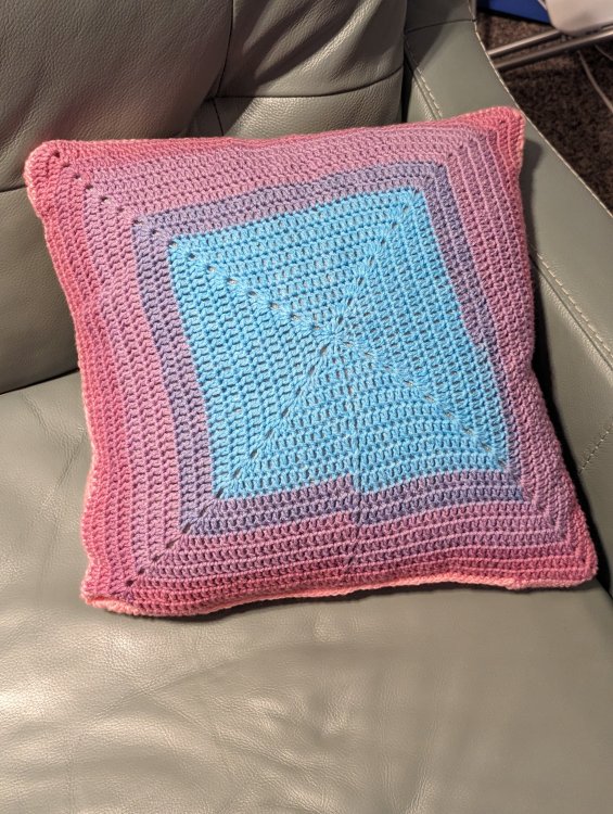 The back portion of a solid granny square crochet pillow cover with blue in the center fading to pink on the edge.