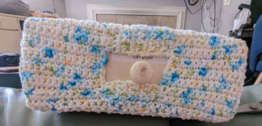 A crochet white drawer cover with blue, yellow, and green flecks in it